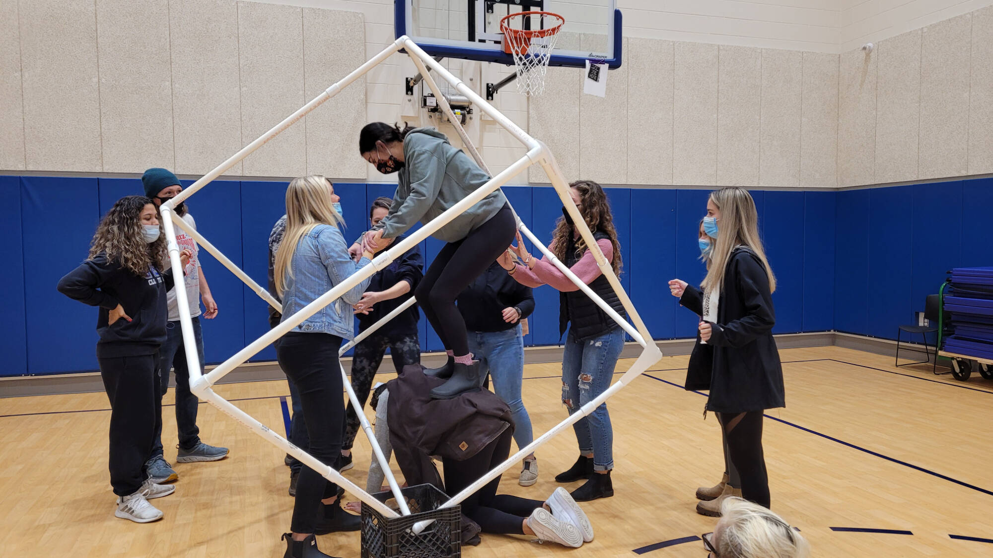 A team-based recreational therapy exercise being performed in a gym with a cube made of PVC pipe